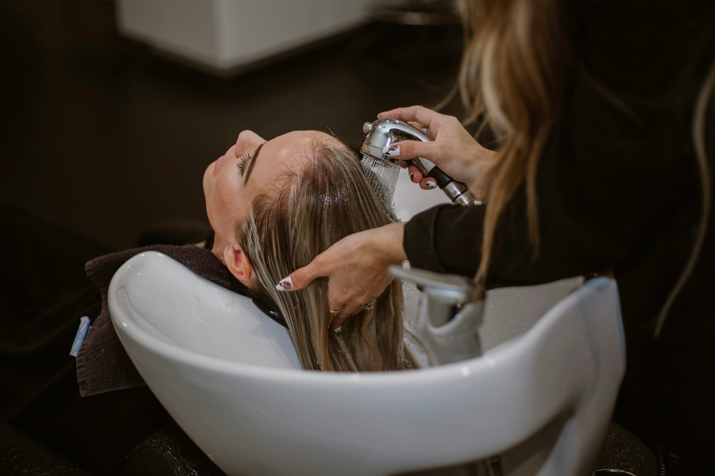 Cabeleireira lava o cabelo de uma cliente no lavatório do salão