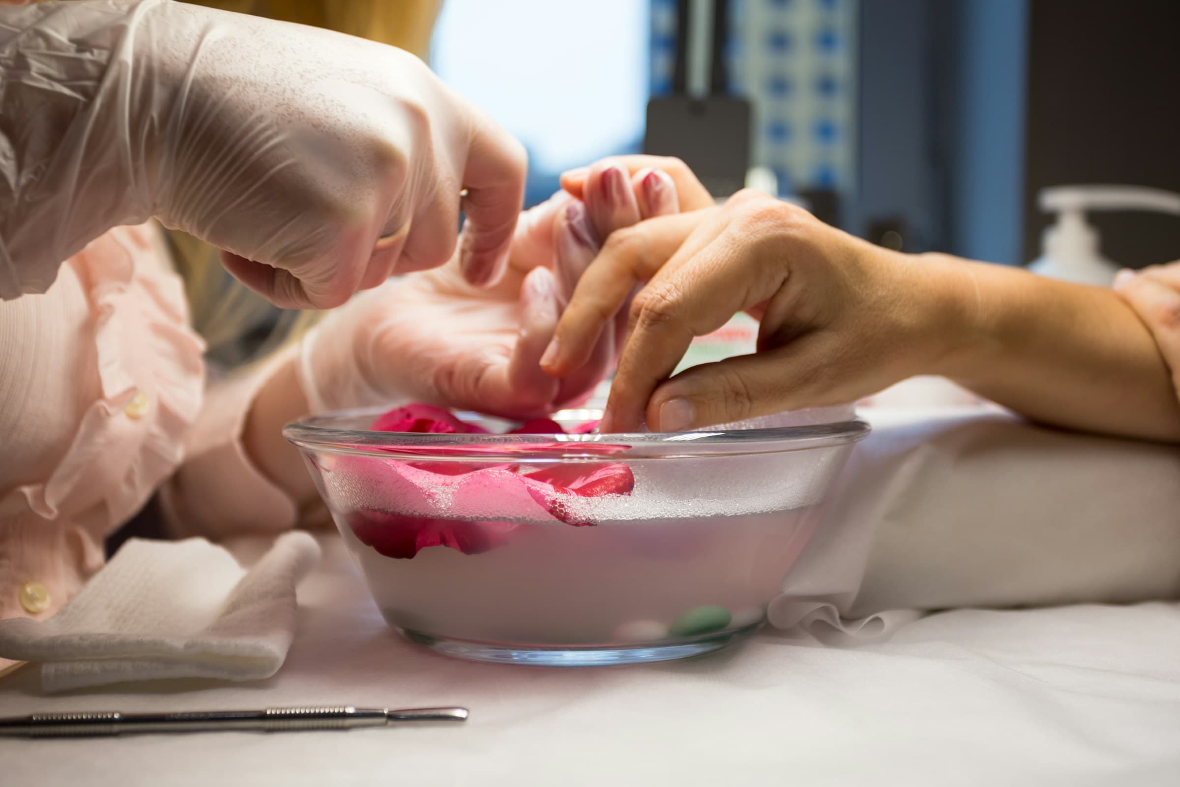Manicure de luvas prepara as unhas da cliente, com os dedos de molho numa tigela com pétalas