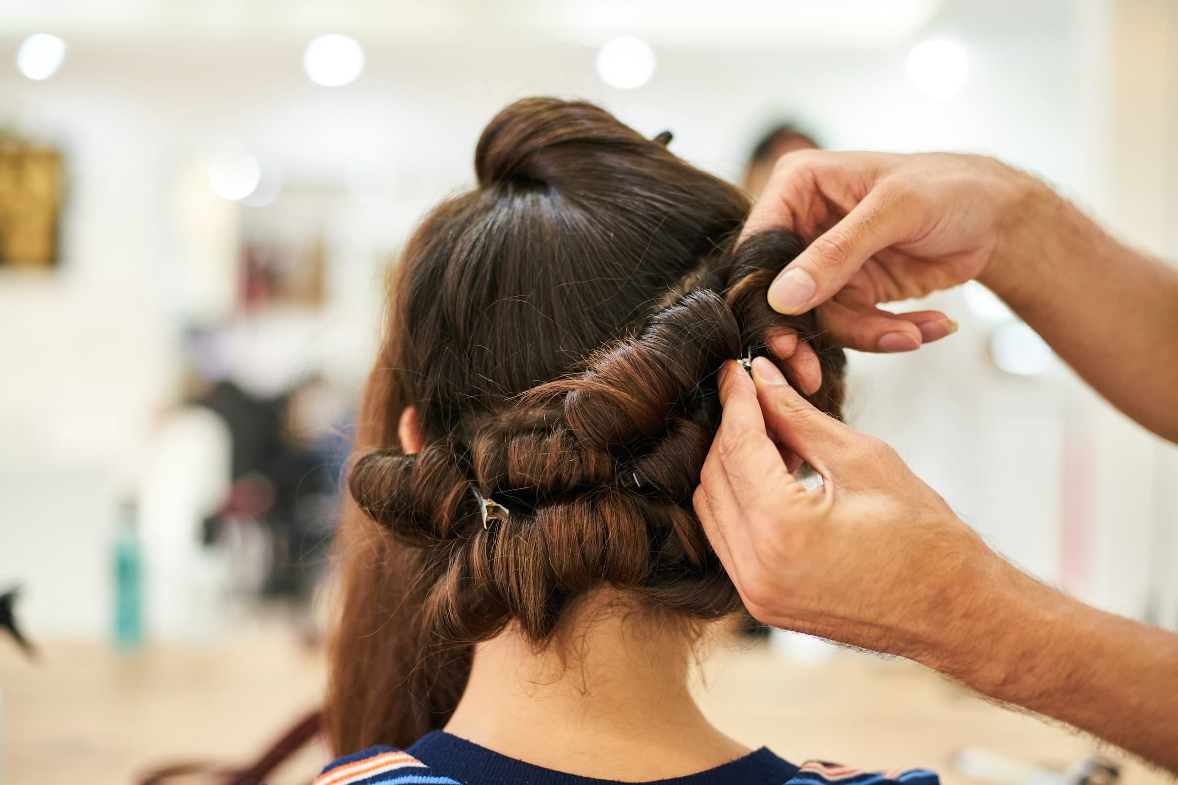 Profissional prende um penteado com grampos no cabelo de uma cliente no salão