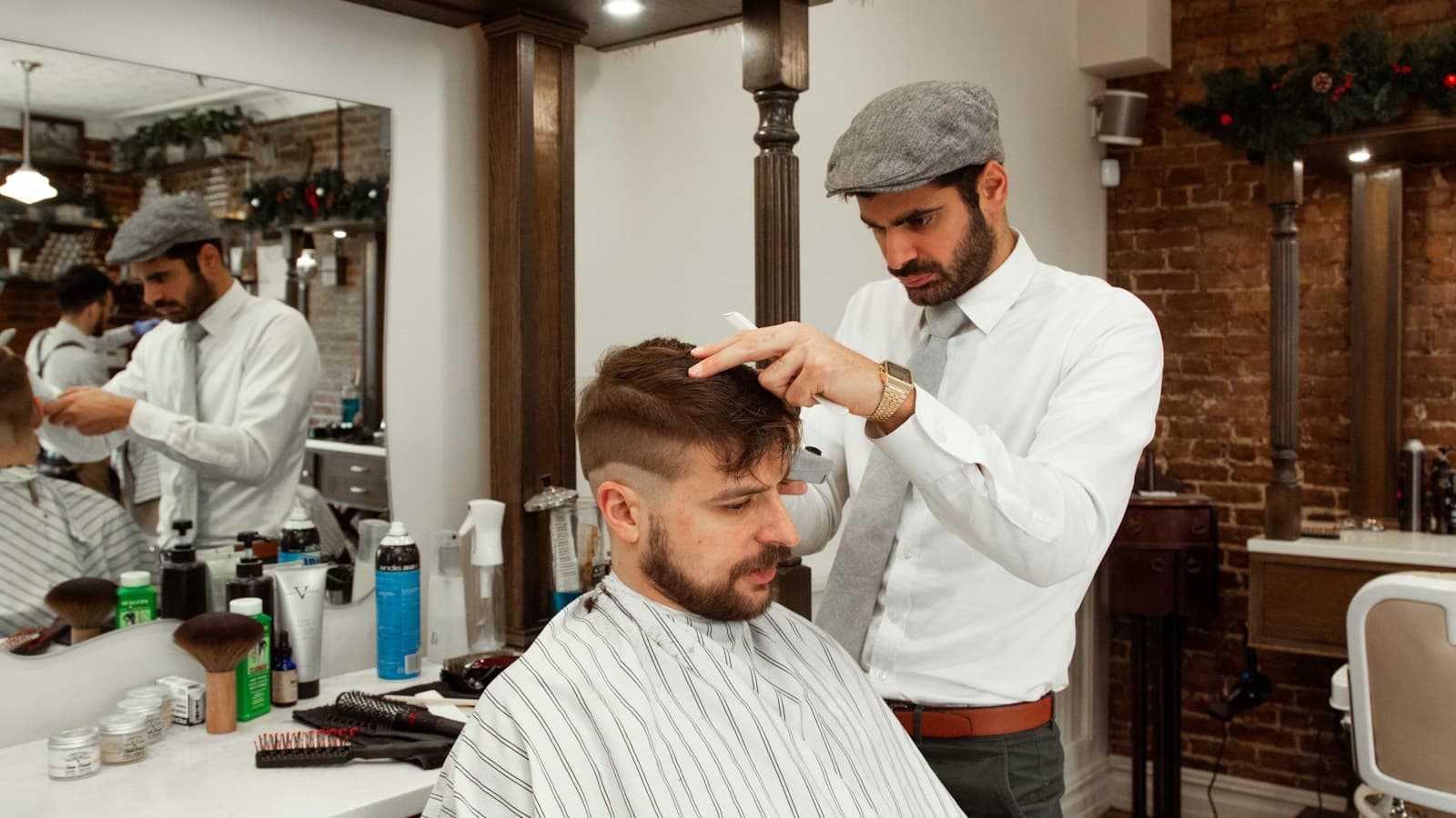 Dois barbeiros atendem clientes lado a lado na mesma barbearia