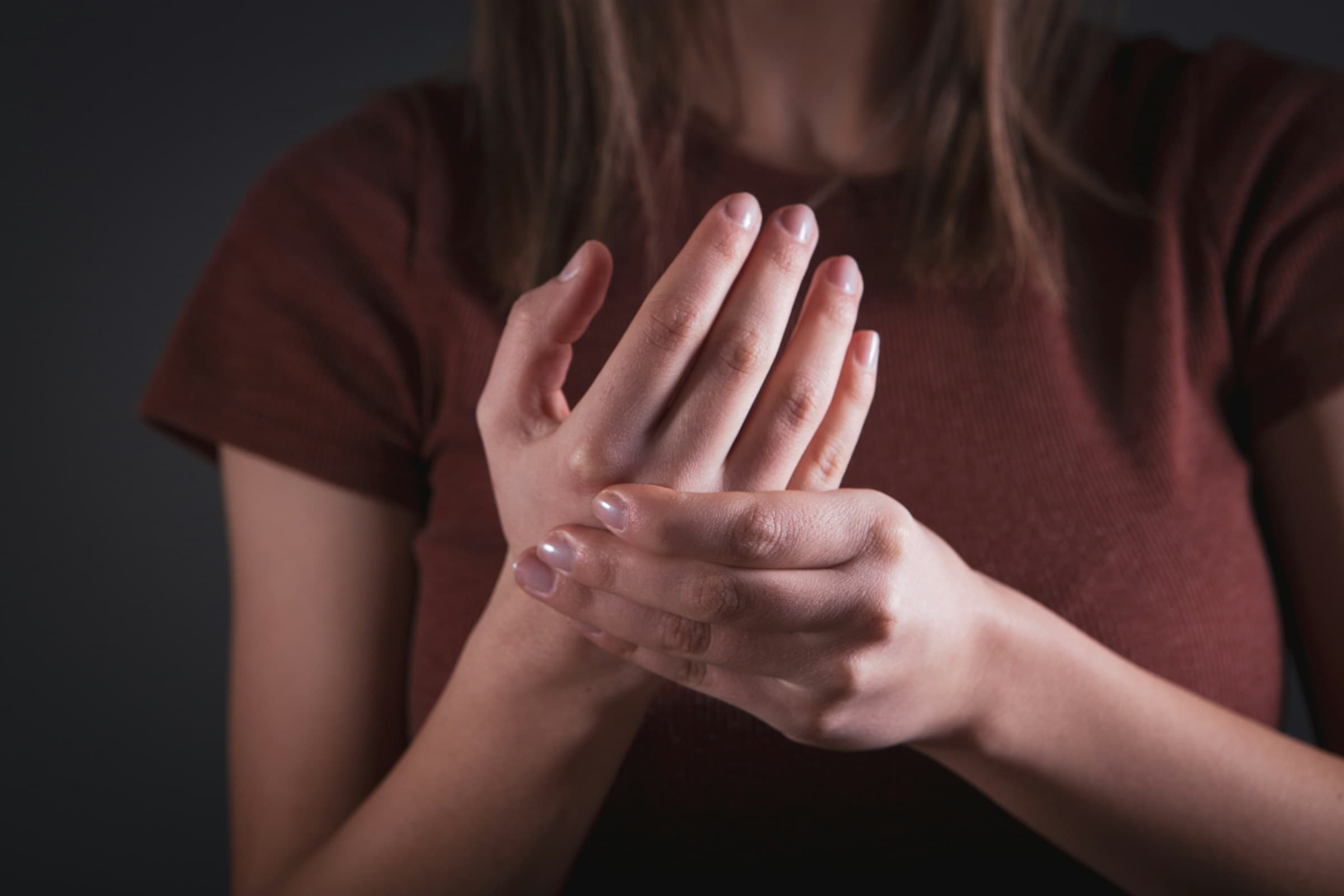 Mulher de unhas pintadas segura e massageia a mão, em fundo escuro