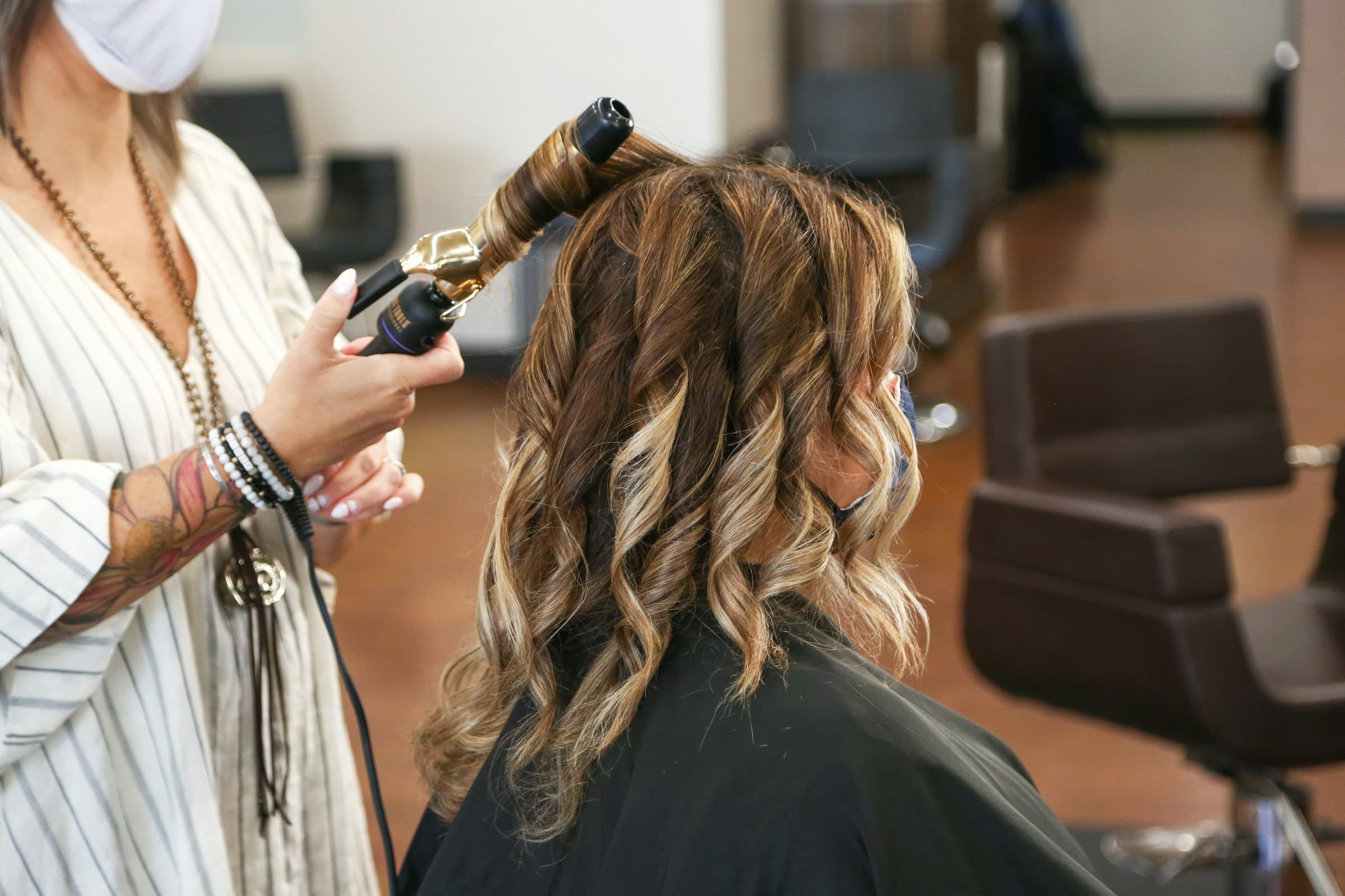 Cabeleireira modela o cabelo de uma cliente com babyliss no salão