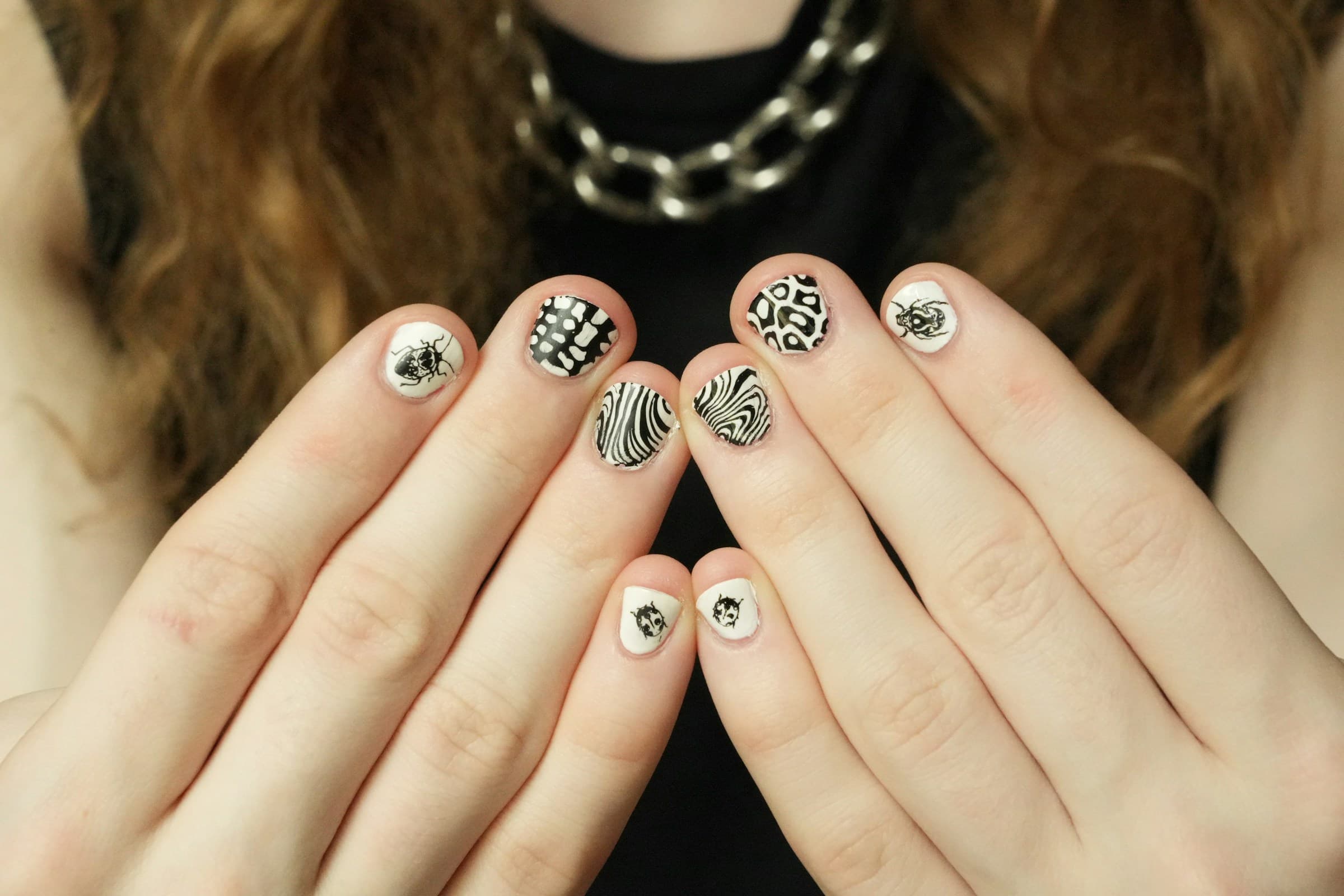 Mãos com unhas curtas decoradas com nail art em preto, branco e prata, uma estampa diferente em cada unha