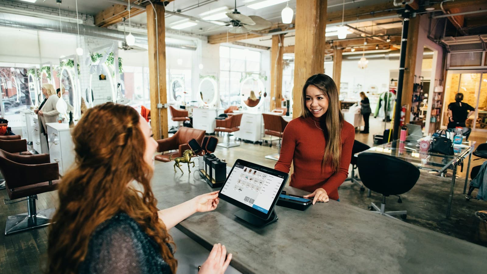 Recepcionista de salão atende uma cliente no balcão com um tablet