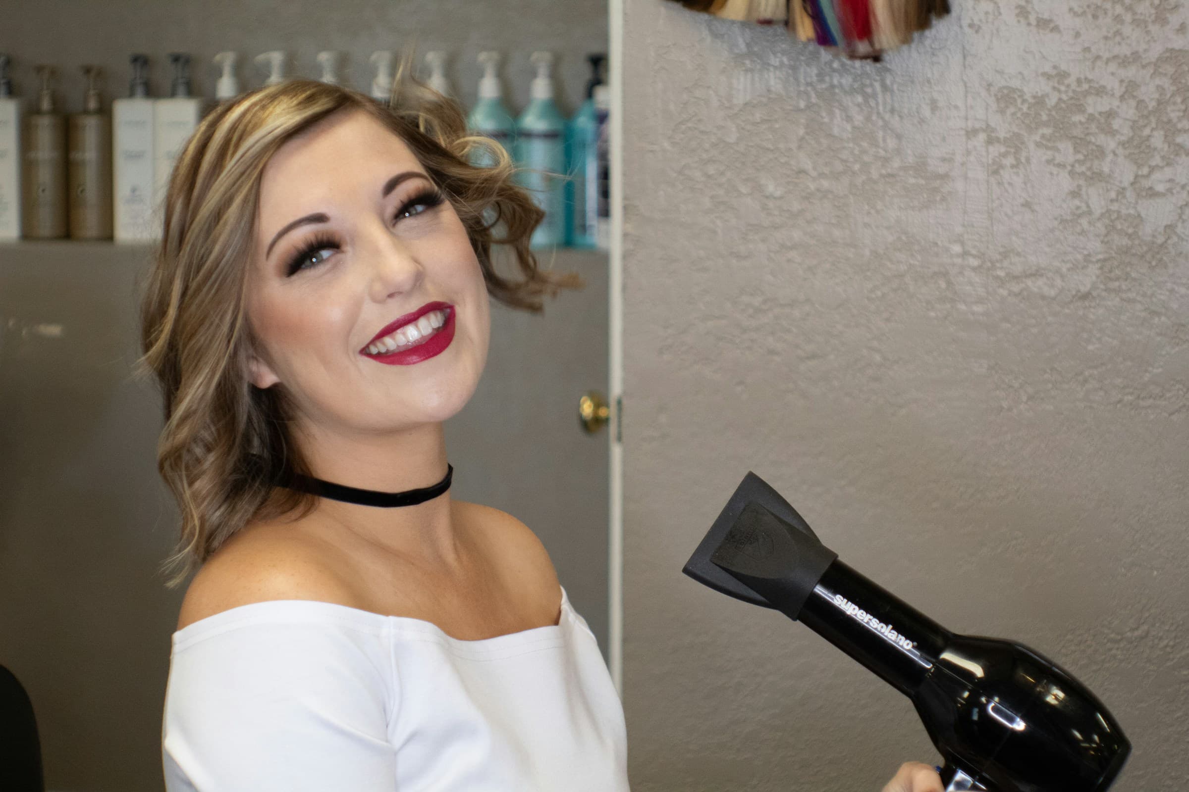 Cliente sorridente com cabelo recém-escovado, ao lado de um secador, no salão de beleza