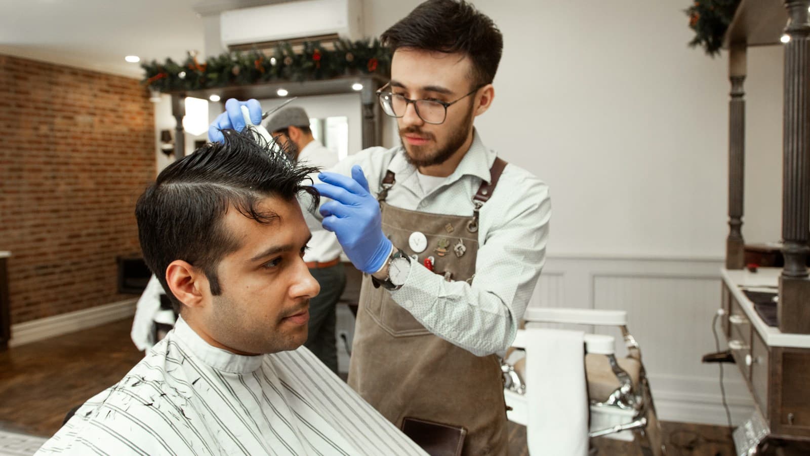 Barbeiro de luvas ajeita o cabelo de um cliente na cadeira da barbearia