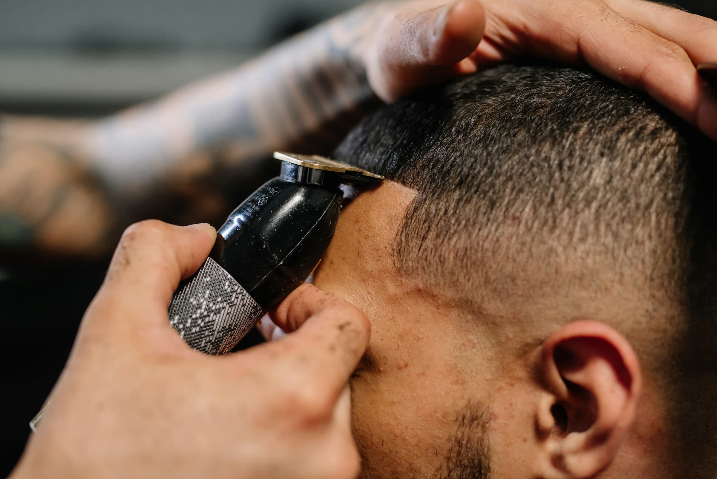 Mãos do barbeiro acertam o contorno do cabelo com a máquina, bem de perto