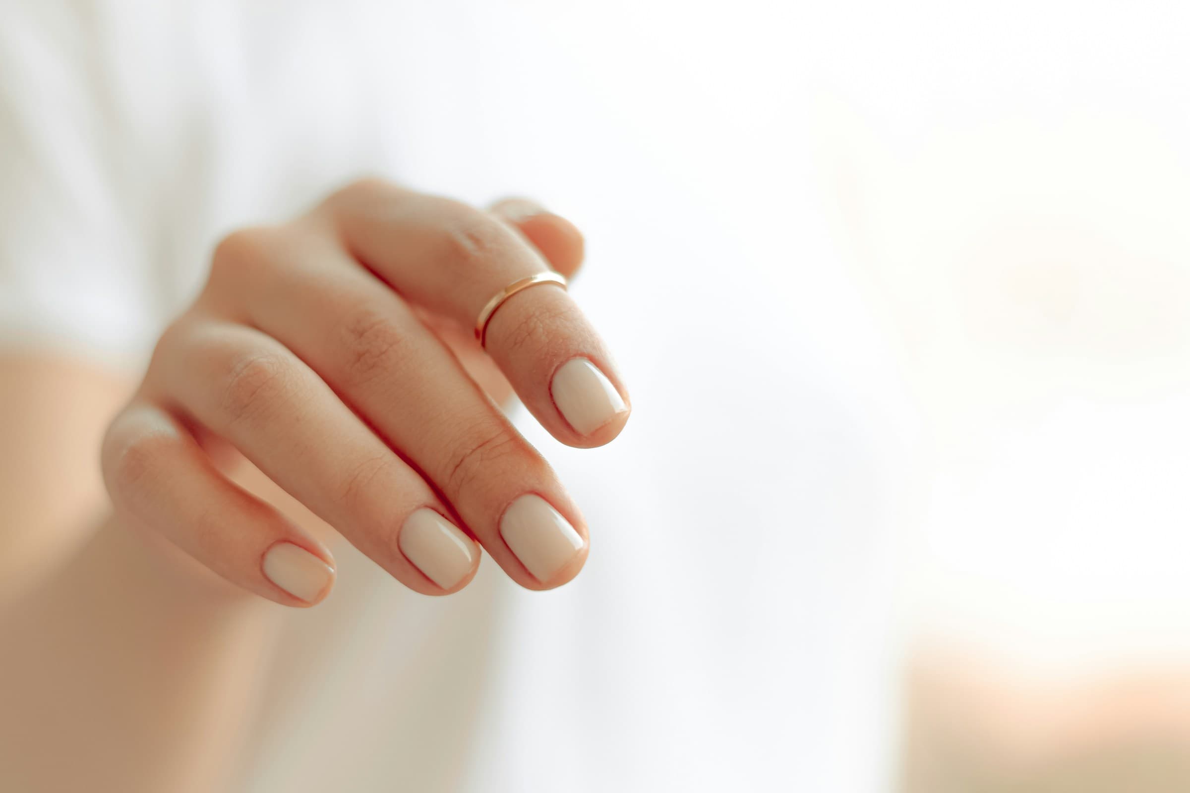 Mão com unhas em gel branco leitoso e acabamento brilhante, sob luz suave