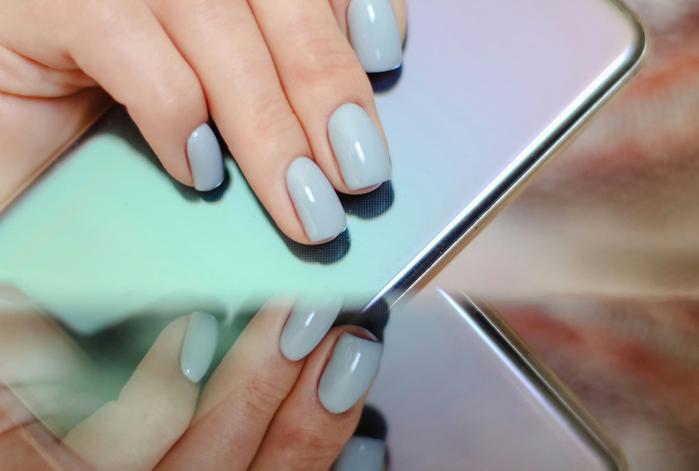 Mãos com unhas esmaltadas em azul-claro seguram um celular
