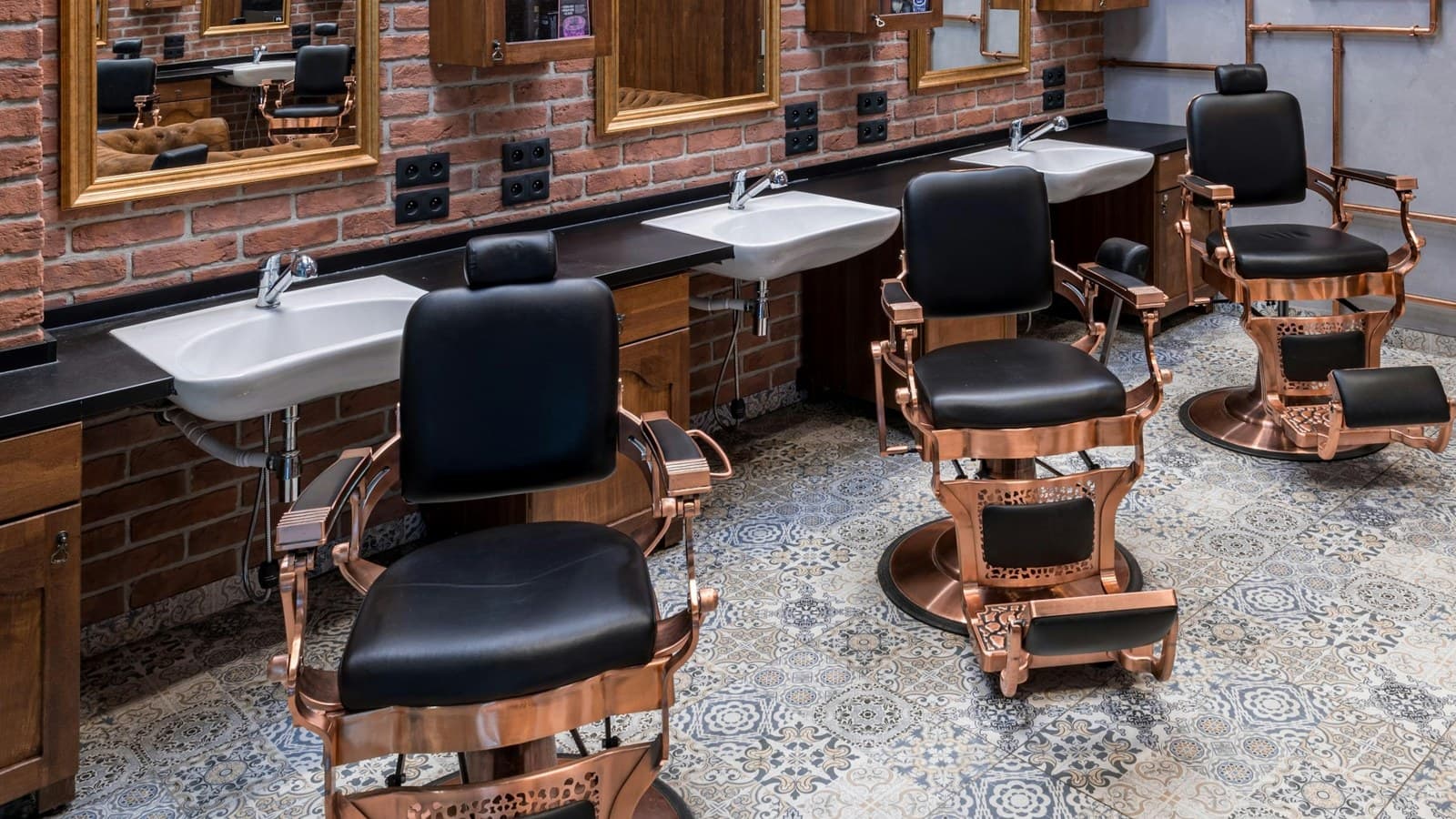 Fileira de cadeiras de barbeiro com lavatórios numa barbearia de parede de tijolos