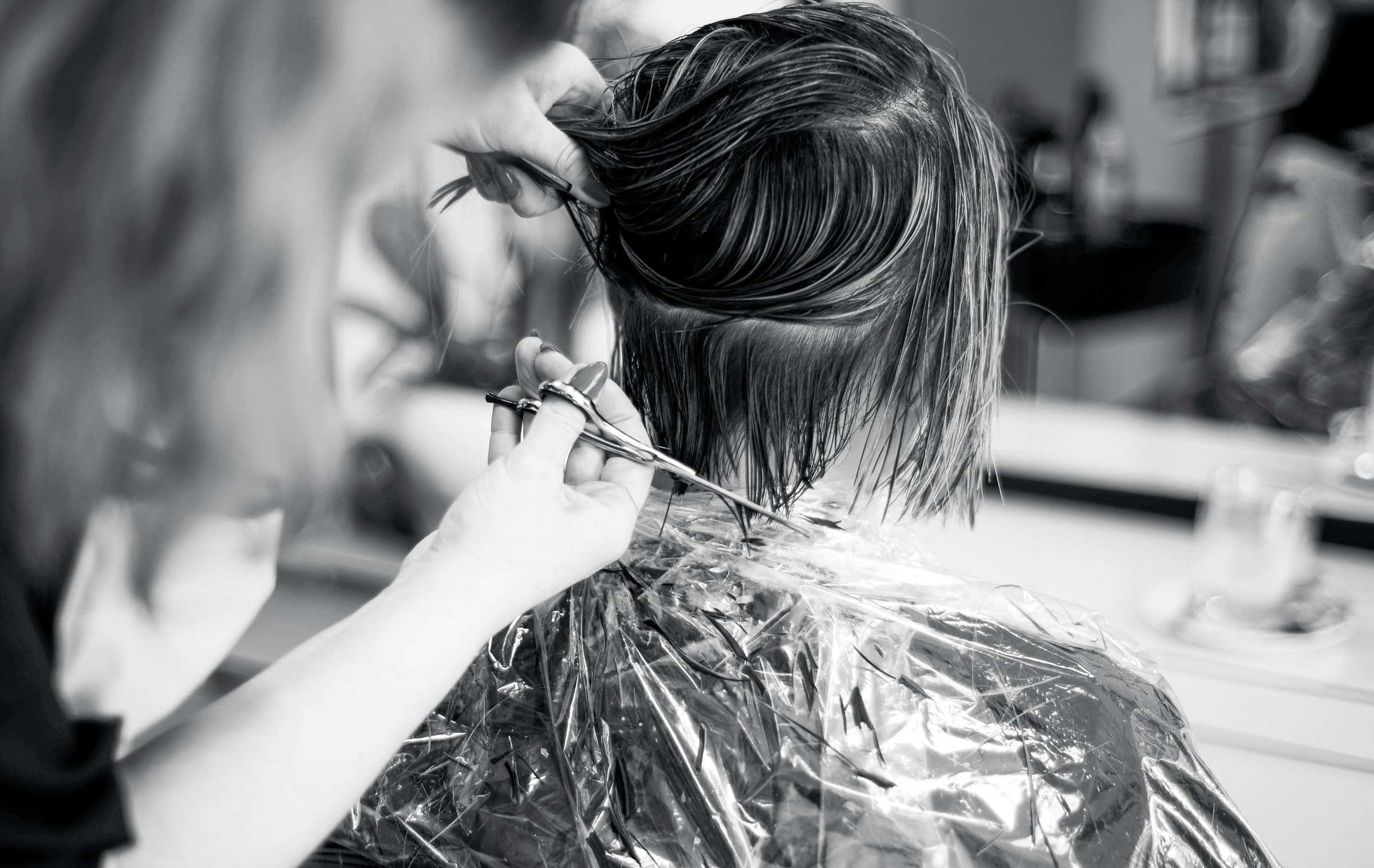 Cabeleireira corta o cabelo de uma cliente com tesoura, em preto e branco