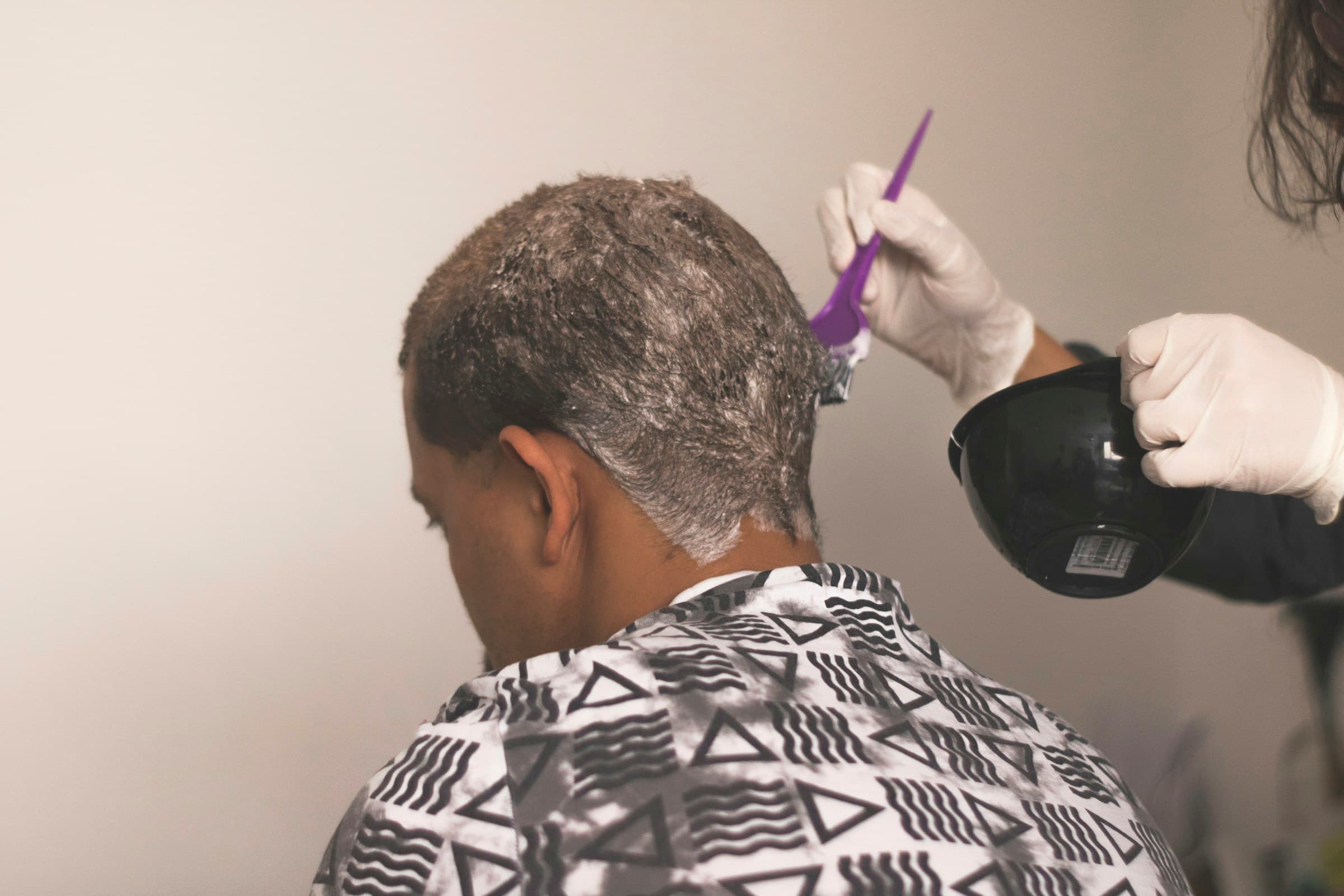 Profissional de luvas aplica tinta com pincel no cabelo de um cliente